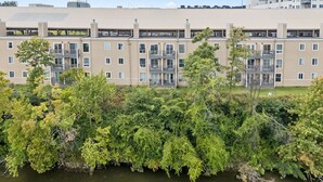 Un edifici residencial de diverses plantes amb balcons, un riu al primer pla i un cel serè.