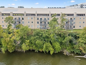 Ein mehrstöckiges Wohngebäude mit Balkonen, im Vordergrund ein Fluss und ein klarer Himmel.