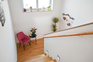 A staircase with a wooden handrail, a red chair, and a small table with a potted plant.