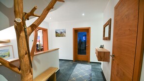 Un pasillo con un banco de madera, una puerta, un espejo y piso de baldosas.