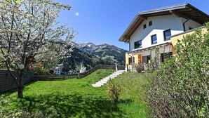 Una casa moderna con una escalera que conduce a una terraza de madera, rodeada de exuberante vegetación y un telón de fondo de montañas.