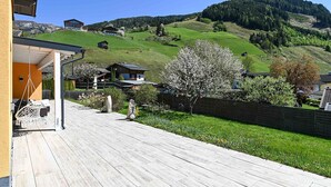Una terraza de madera que conduce a una casa con vistas a una ladera verde y un árbol en flor.