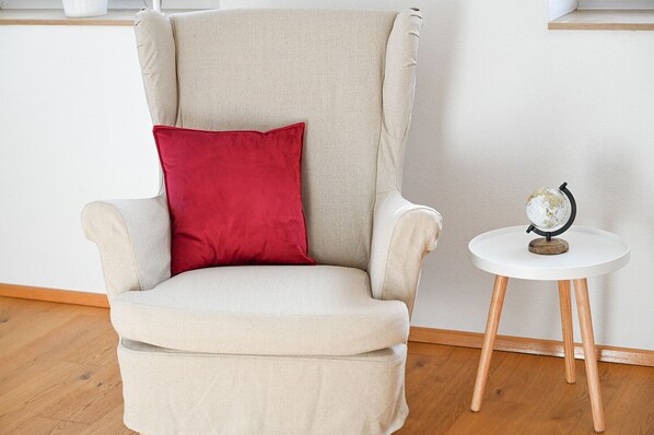 A chair with a red pillow, a small round table with a globe, and wooden legs.