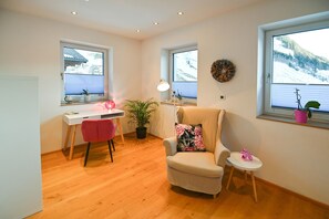 Une pièce comprenant un bureau, une chaise, un fauteuil et deux fenêtres donnant sur un paysage enneigé.
