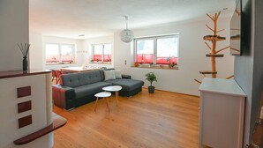 Una sala de estar moderna con un sofá gris, dos mesitas blancas, una mesa de centro de madera y una planta en maceta.