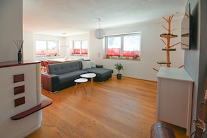 Ein stilvolles Wohnzimmer mit einem grauen Sofa, zwei weißen Beistelltischen, einem Holztisch und einem Blumentopf.