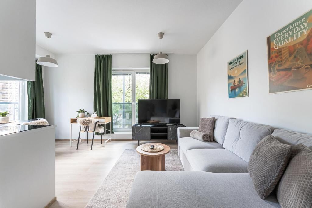 Een moderne woonkamer met een bank, een televisie, een eethoek met een tafel en stoelen, en een groot raam met gordijnen.