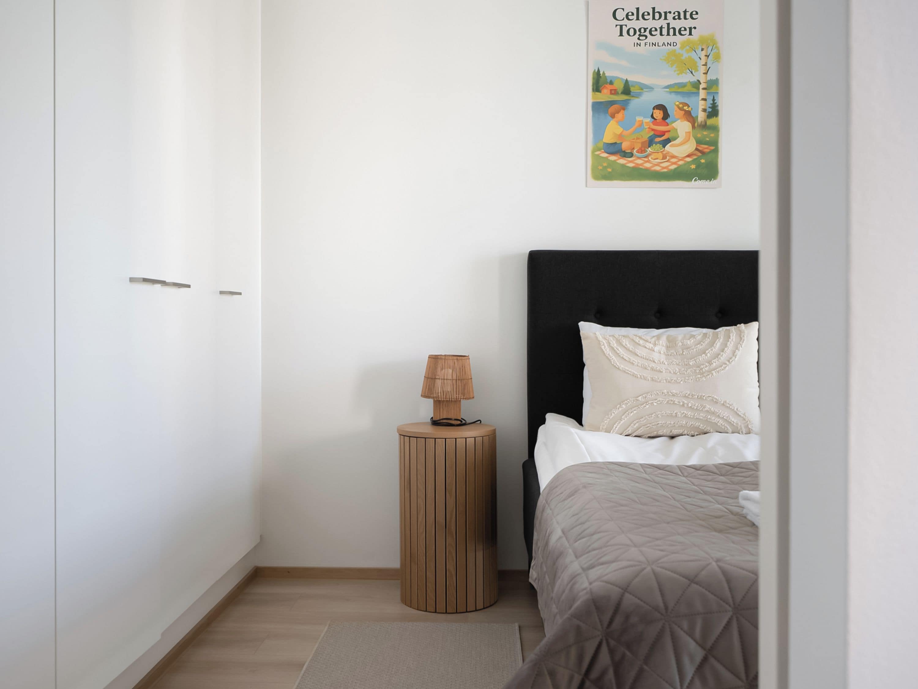 Un dormitorio con una cama, una lámpara de noche, un póster en la pared y suelo de madera.
