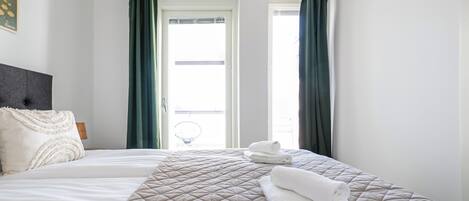 A hotel room with a bed, two pillows, a folded towel, and a view of the outside.