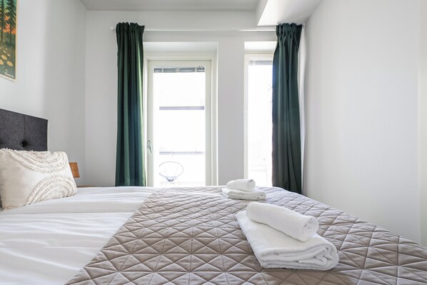 A hotel room with a bed, two pillows, a folded towel, and a view of the outside.