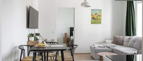 A modern living space with a dining area, a sofa, a TV mounted on the wall, and a poster on the wall.