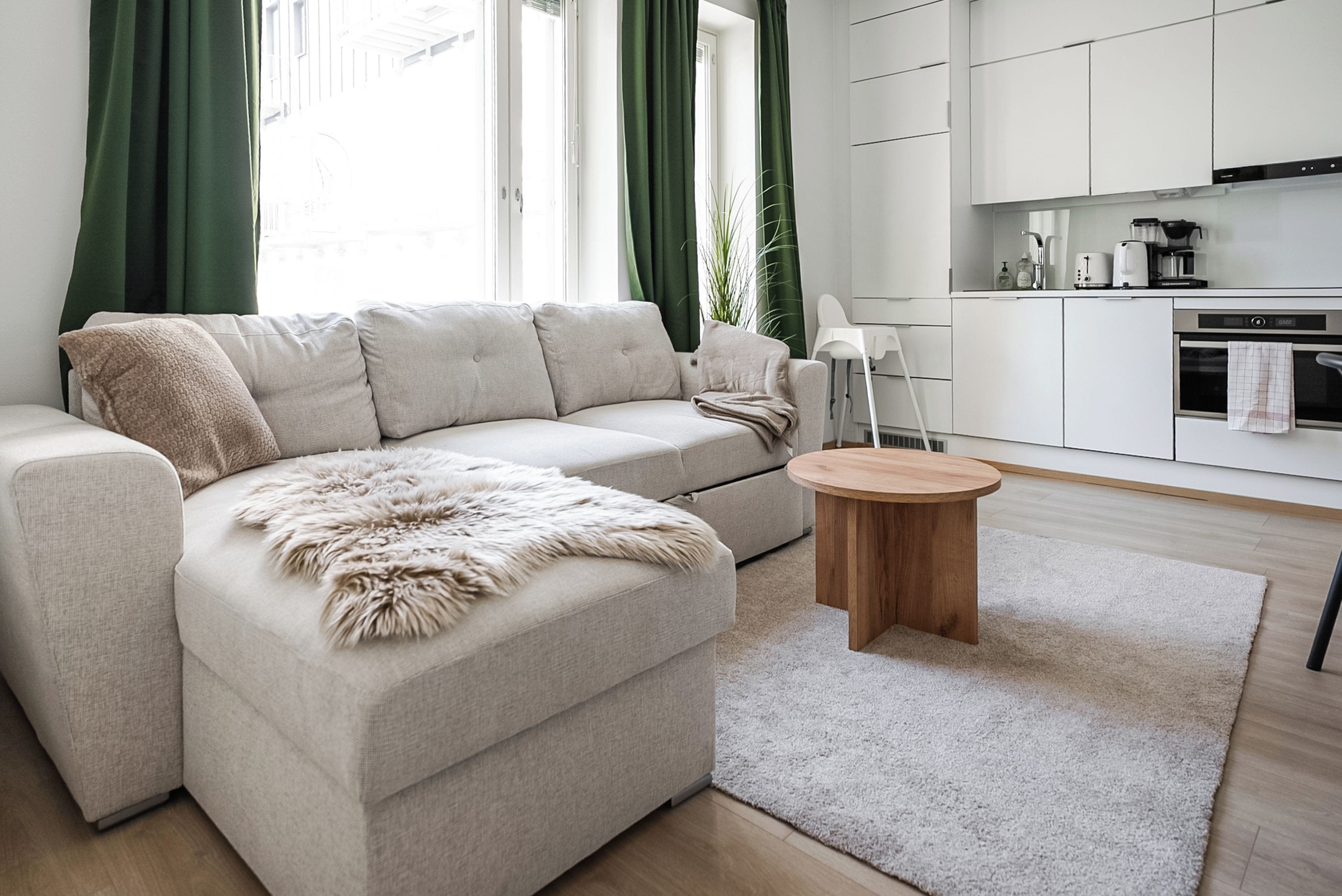 Una sala de estar moderna con un sofá, una mesa de centro redonda de madera y una zona de cocina con armarios y electrodomésticos.