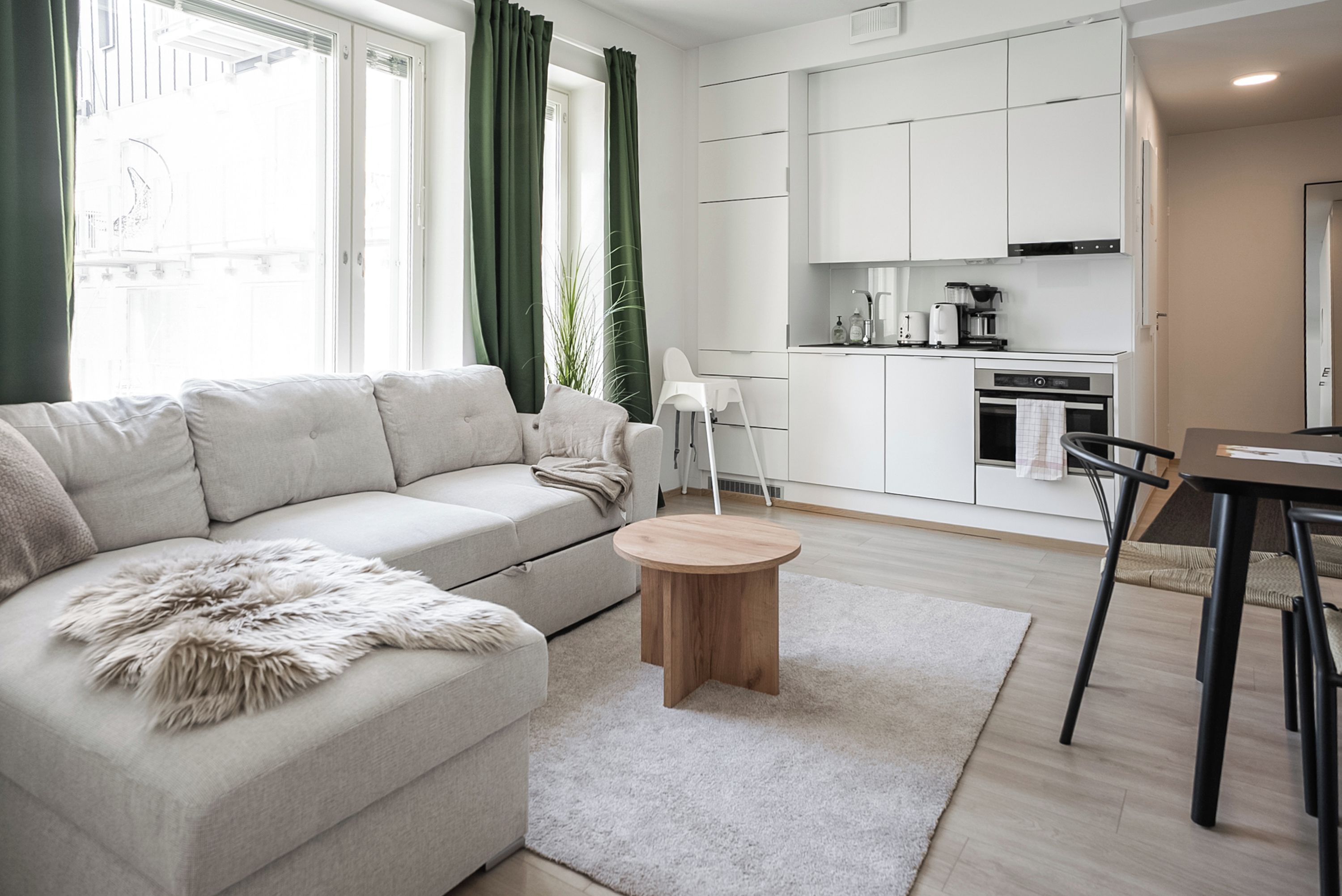 Una sala de estar moderna con un sofá, una mesa de centro redonda de madera y una cocina con armarios y electrodomésticos.