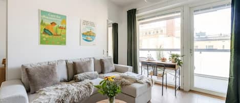 Uma sala de estar moderna com um sofá cinza, uma mesa de centro com um vaso de flores e vista para a cidade através de grandes janelas.