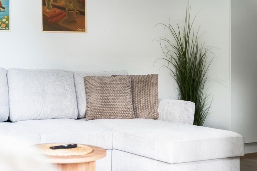 Un salon moderne avec un canapé blanc, une petite table d’appoint en bois et une grande plante verte.