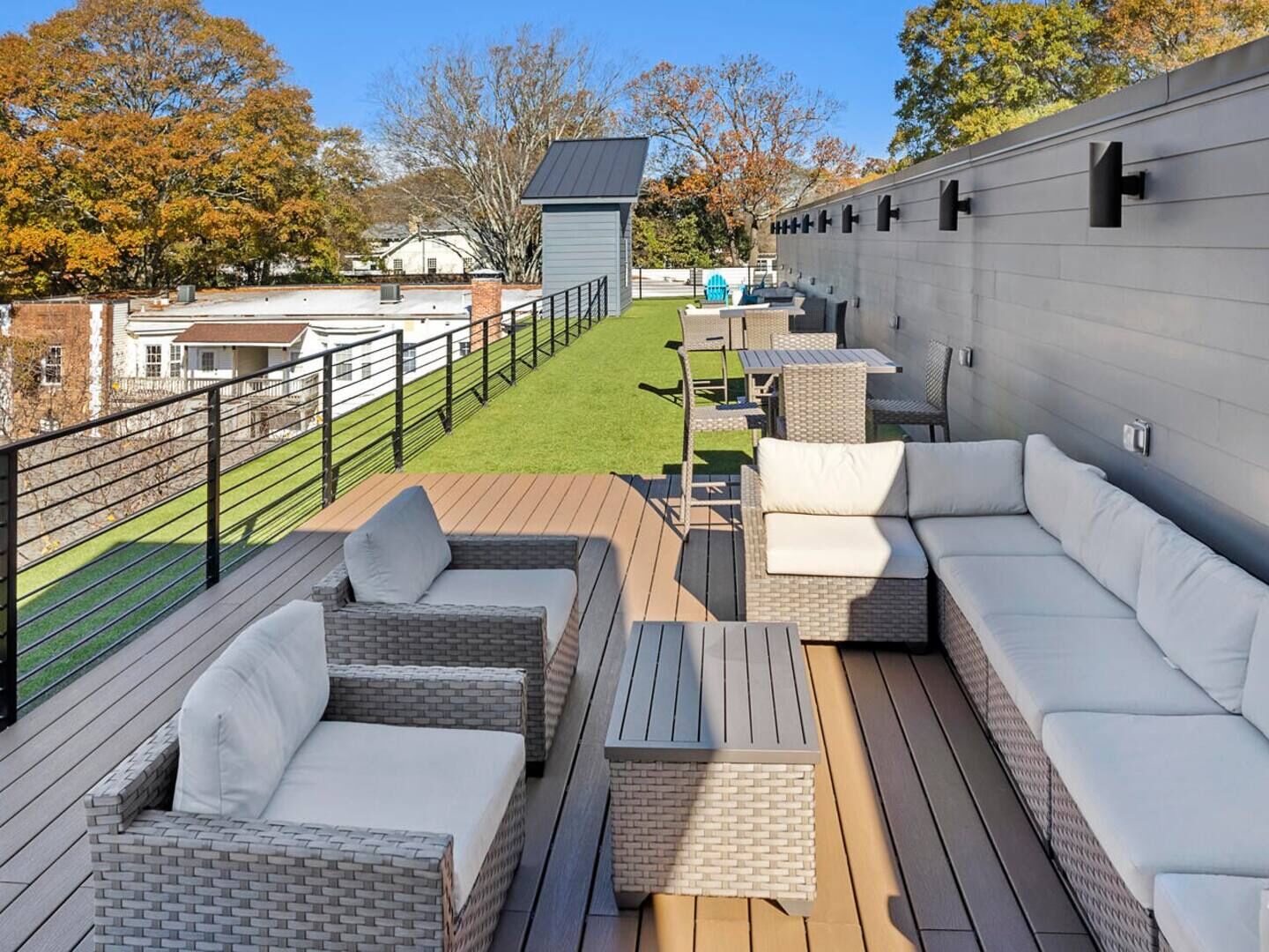 A rooftop patio with wicker furniture, a small table, and a view of a green lawn and buildings in the background.