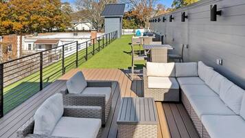 A rooftop patio with wicker furniture, a small table, and a view of a green lawn and buildings in the background.