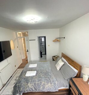 Un dormitorio con cama, televisor, mesita de noche y perchero.