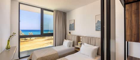 A hotel room with two beds, a large window with a beach view, and a vase with flowers on a table.