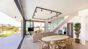 Ein modernes Wohnzimmer mit einer großen Couch, einem Esstisch mit Stühlen, einem Fernseher und einer Treppe zu einer oberen Ebene.