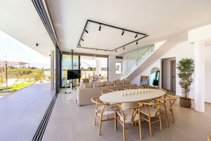 Ein modernes Wohnzimmer mit einer großen Couch, einem Esstisch mit Stühlen, einem Fernseher und einer Treppe zu einer oberen Ebene.