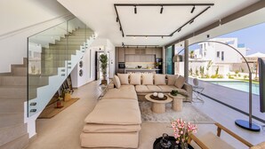Ein moderner Wohnraum mit Treppe, einer Sofagarnitur, einem Essbereich und Blick ins Freie.