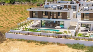 Ein modernes, zweistöckiges Haus mit Pool auf dem Dach, Sitzgelegenheiten im Freien und einem angelegten Garten.