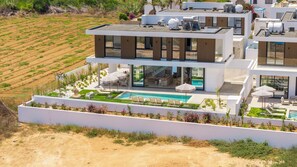 Ein modernes, zweistöckiges Haus mit Pool auf dem Dach, Sitzgelegenheiten im Freien und einem angelegten Garten.