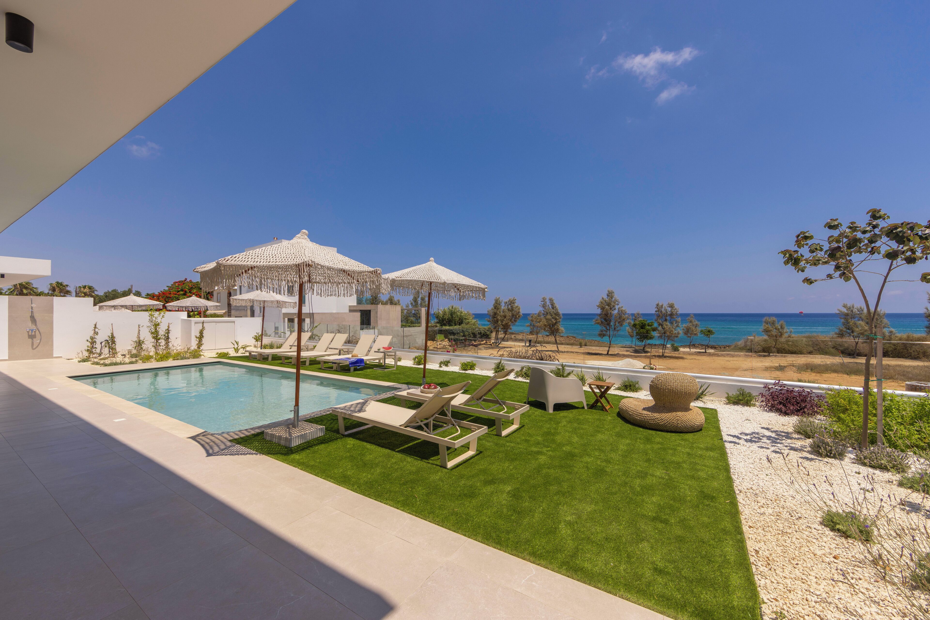 A poolside area with lounge chairs, umbrellas, and a view of the sea.