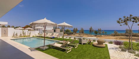 A poolside area with lounge chairs, umbrellas, and a view of the sea.
