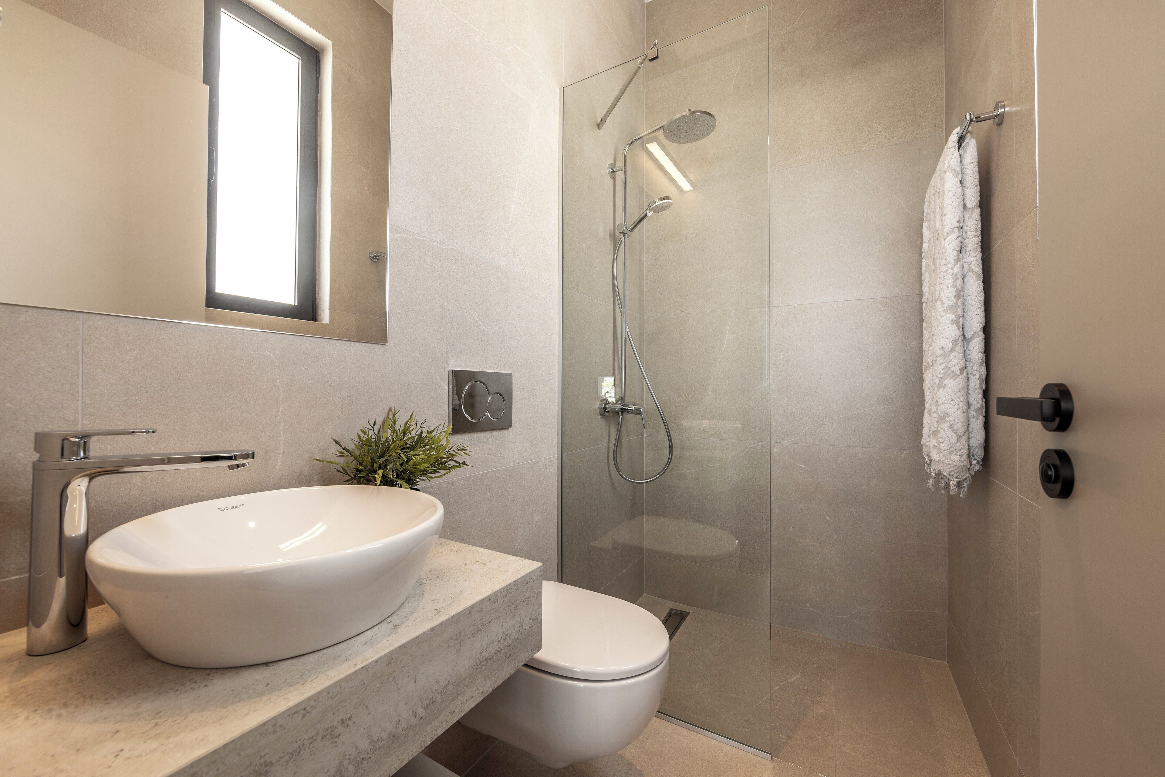 Ein modernes Badezimmer mit Waschbecken, Toilette und Dusche, alles in Weiß.