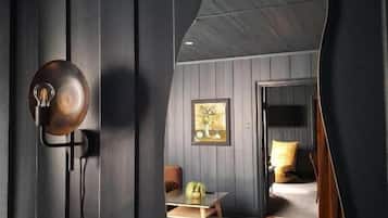 Une pièce avec un miroir incurvé, une lampe, un tableau encadré, un lit et une petite table sur laquelle se trouve un vase.