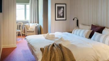 Une chambre d’hôtel avec un grand lit, une chaise, un tableau encadré au mur et une fenêtre avec des rideaux.
