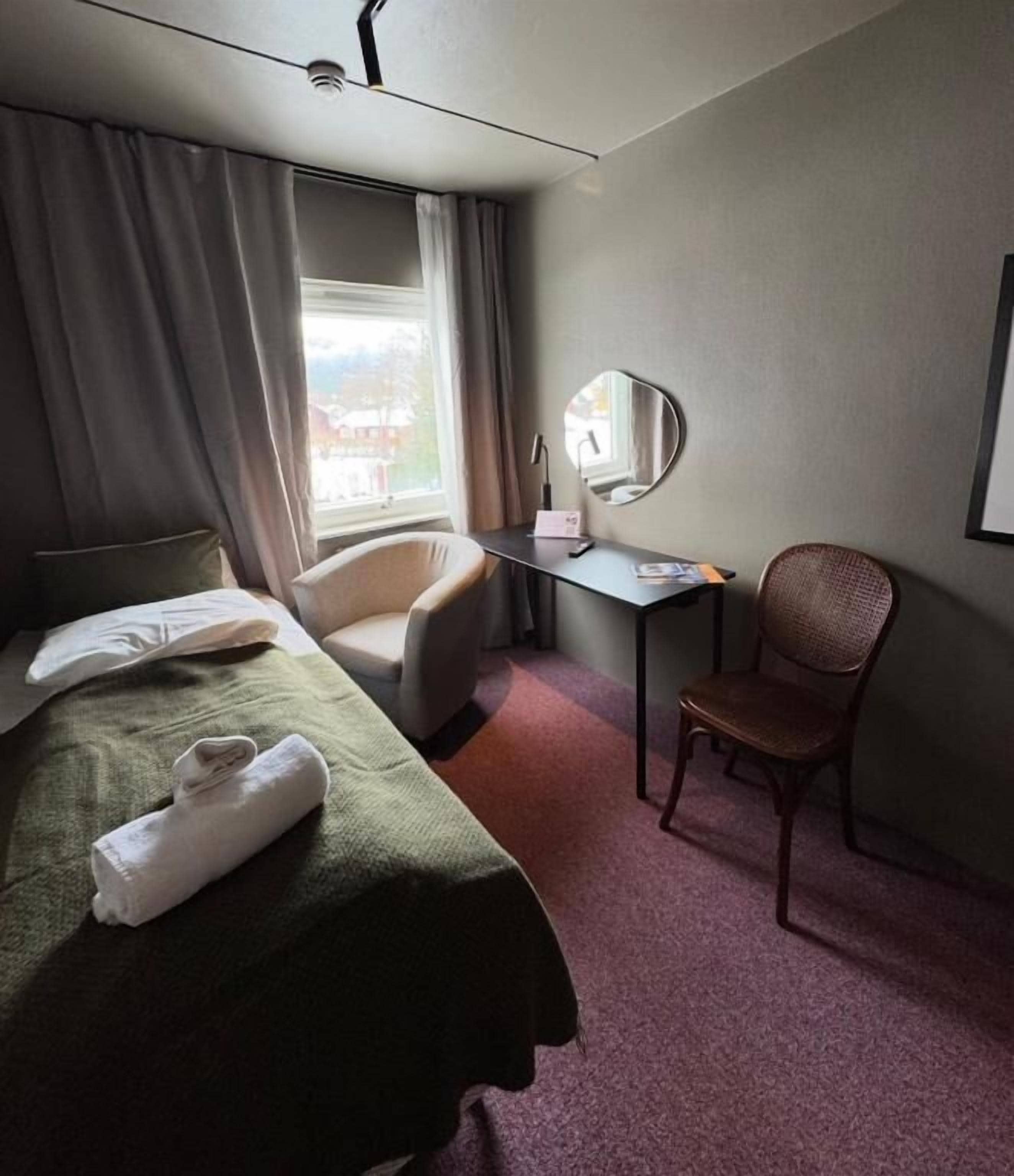 Una camera d'albergo con un letto, una scrivania, una sedia e una finestra.