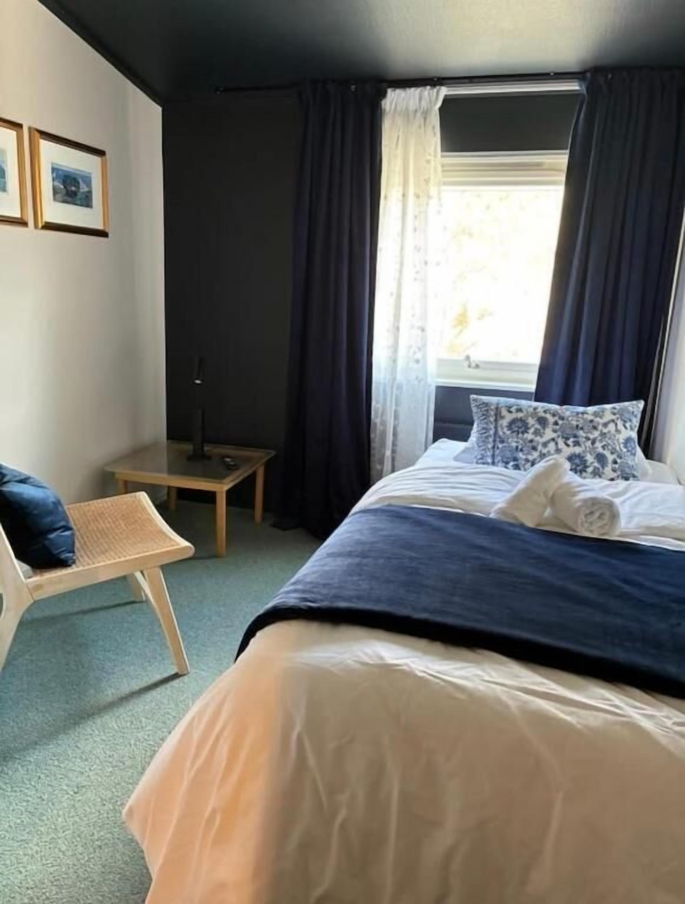 Una habitación de hotel con una cama, una silla, una mesita y un ventanal con cortinas.