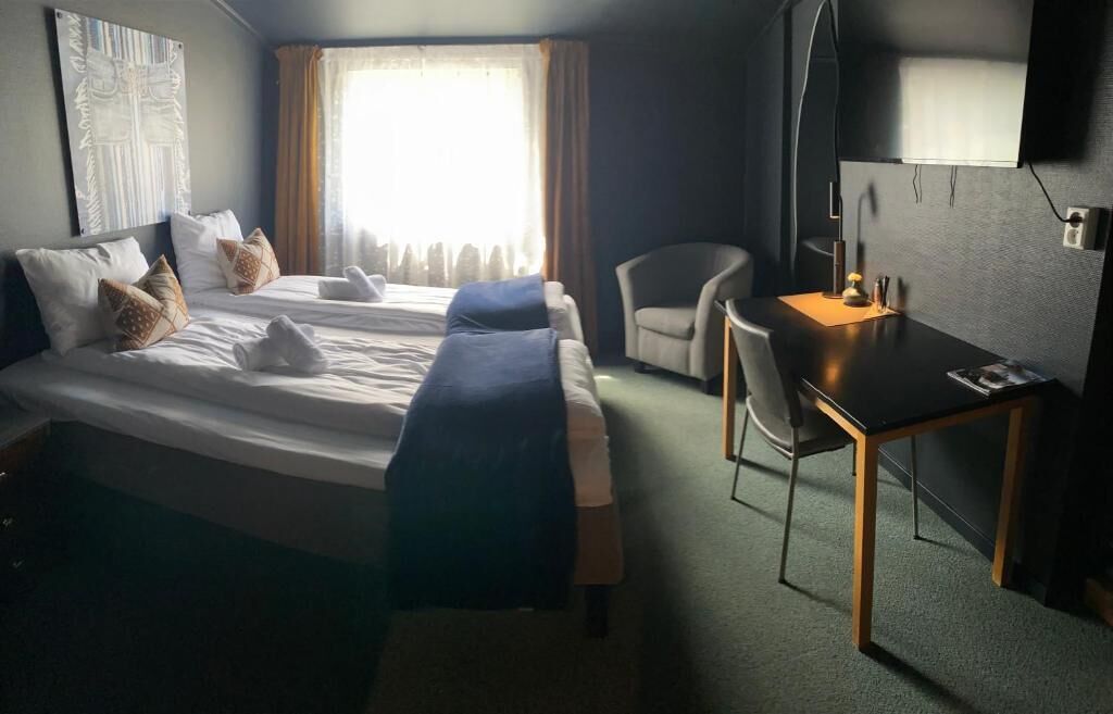 A hotel room with two beds, a desk, a chair, and a TV.
