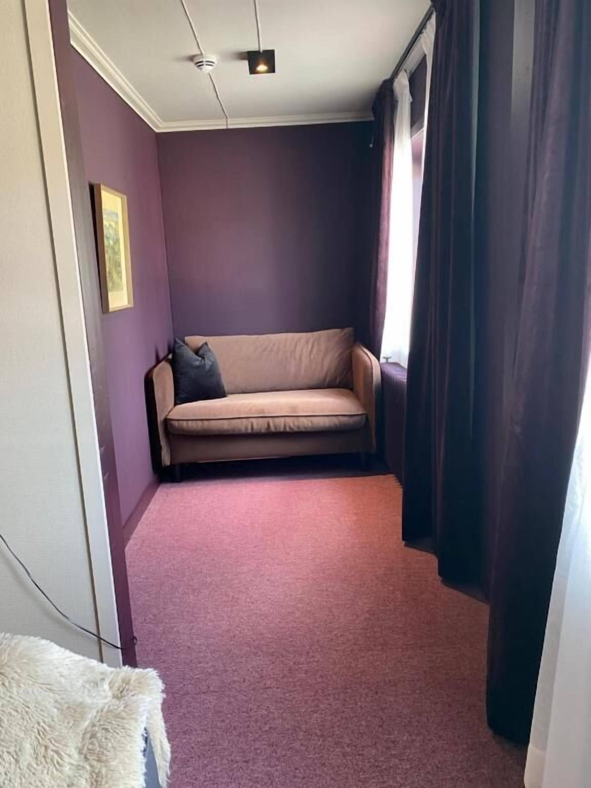Una habitación con pared morada, sofá color beige y suelo alfombrado.