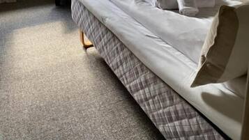 Een enkel bed met hoofdeinde, nachtkastje en stoel in een kamer met raam en een lijst met foto.