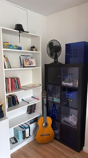 A room with a white bookshelf filled with books and a guitar, a black cabinet with glass doors, and a black fan on top. - Stylish two bedrooms apartment between King's Cross St Pancras and Russel Square (London)
