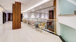 A modern hotel corridor with a row of tables and chairs, a decorative column, and a glass partition.