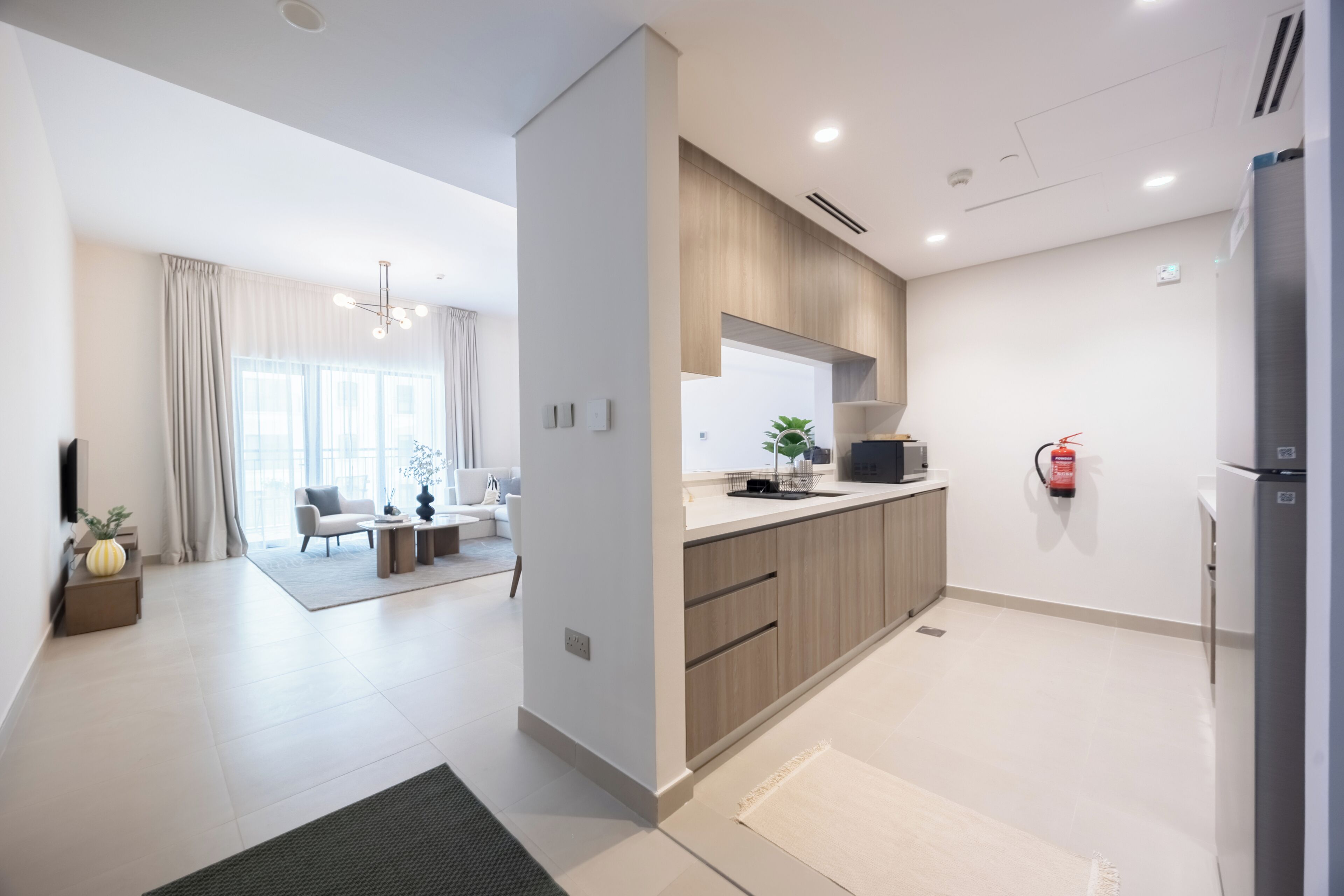 A modern kitchen with a built-in microwave, a refrigerator, and a fire extinguisher on the wall.