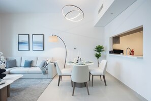 A modern living room with a sofa, a dining table with chairs, and a kitchen area with a window. - Bloomfields 1BR in Fairways 3- YGC (Abu Dhabi)