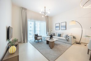 Una sala de estar moderna con un sofá, un sillón, una mesa de centro y un televisor sobre un mueble.