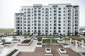 A multi-story residential building with balconies, a landscaped courtyard, and a view of the surrounding area. - Bloomfields 1BR in Fairways 3- YGC (Abu Dhabi)