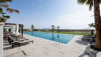 A swimming pool with lounge chairs and umbrellas, surrounded by palm trees and a clear sky.
