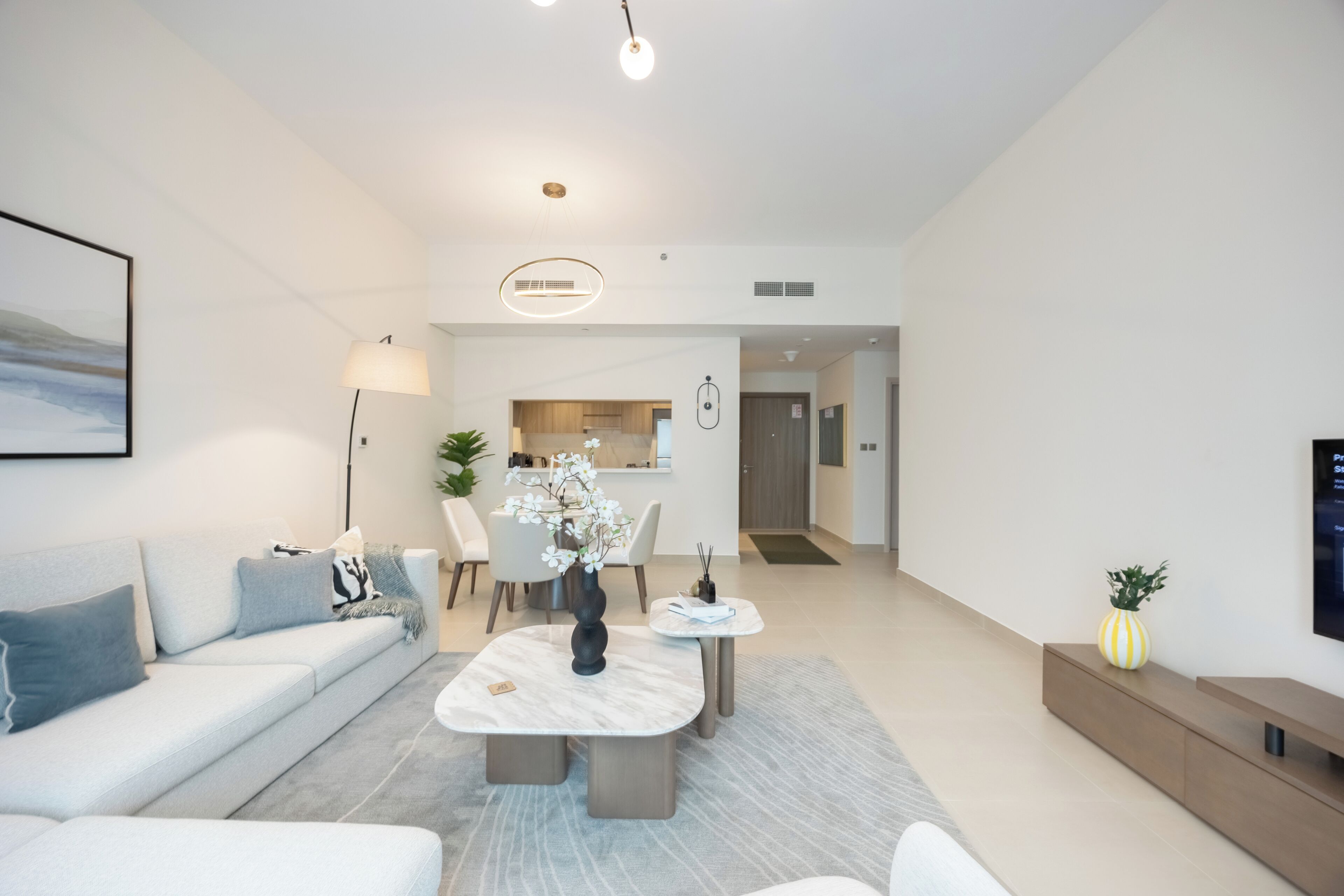 A modern living room with a sofa, coffee table, and a dining area with chairs and a vase of flowers.