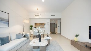 A modern living room with a sofa, coffee table, and a dining area with chairs and a vase of flowers. - Bloomfields 1BR in Fairways 3- YGC (Abu Dhabi)