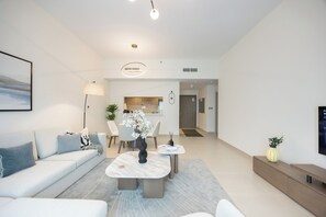 A modern living room with a sofa, coffee table, and a dining area with chairs and a vase of flowers. - Bloomfields 1BR in Fairways 3- YGC (Abu Dhabi)