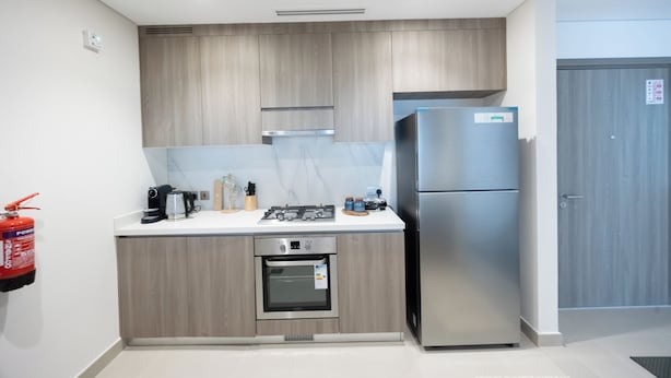 A modern kitchen with wooden cabinets, a stainless steel refrigerator, a built-in oven, and a gas stove. - Bloomfields 1BR in Fairways 3- YGC (Abu Dhabi)