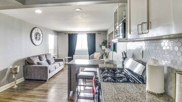 A modern kitchen with a gas stove, a dining area with a sofa, and a living room with a large clock.